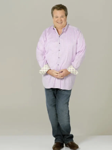 Cameron tucker from Modern Family with his hands crossed, smiling at the camera. 